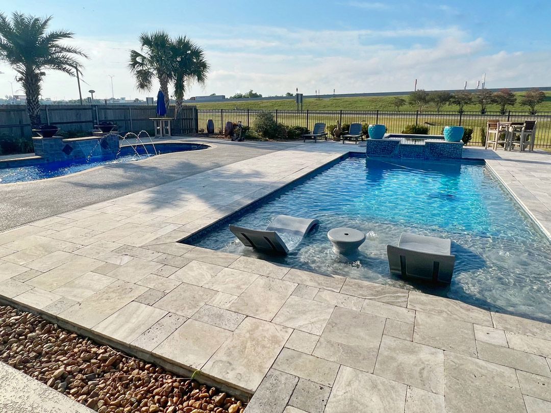 Two swimming pools with wide travertine decking, in-water loungers, palm trees and an open field behind.