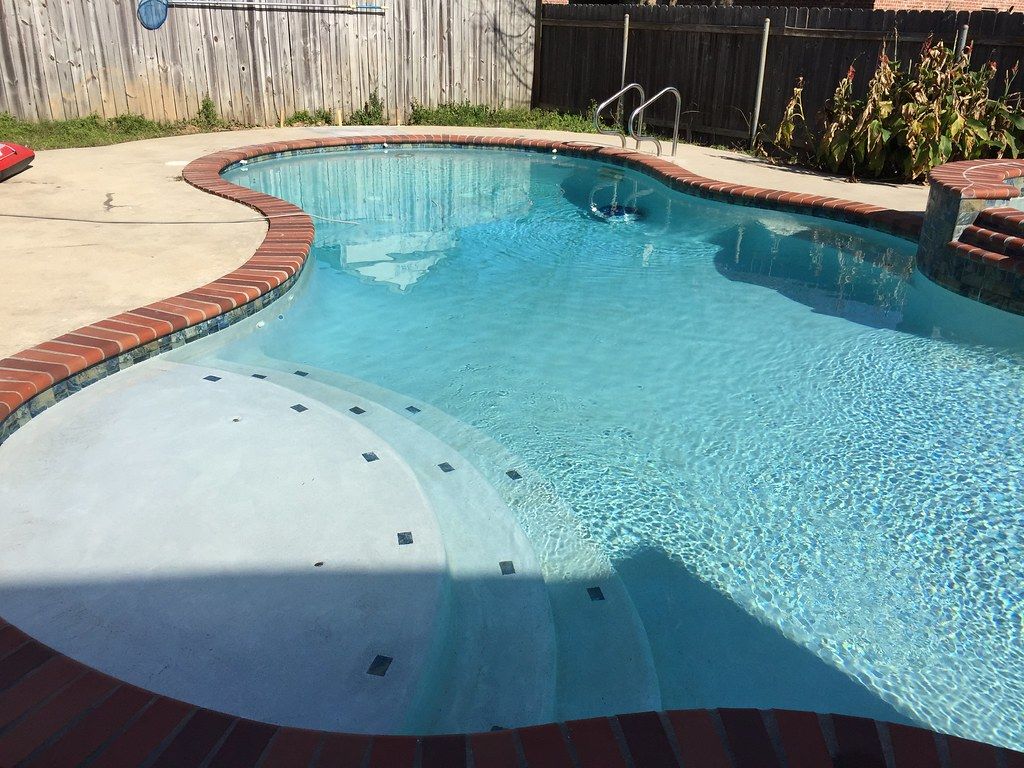 A kidney-shaped pool after renovation: smooth new plaster and clean blue water.